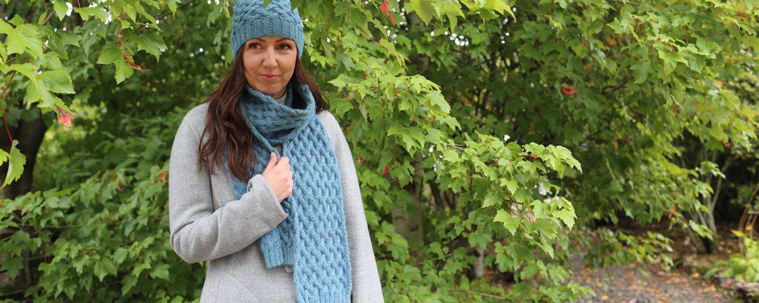 Woman in blue alpaca scarf and hat by some trees